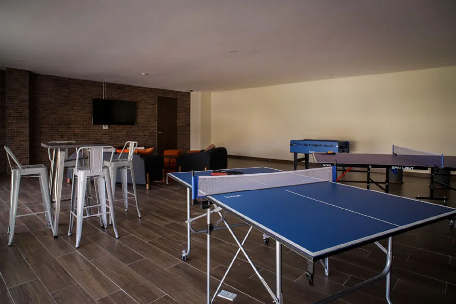 Salón de juegos con mesa de ping pong, futbolito y mesas altas con bancos