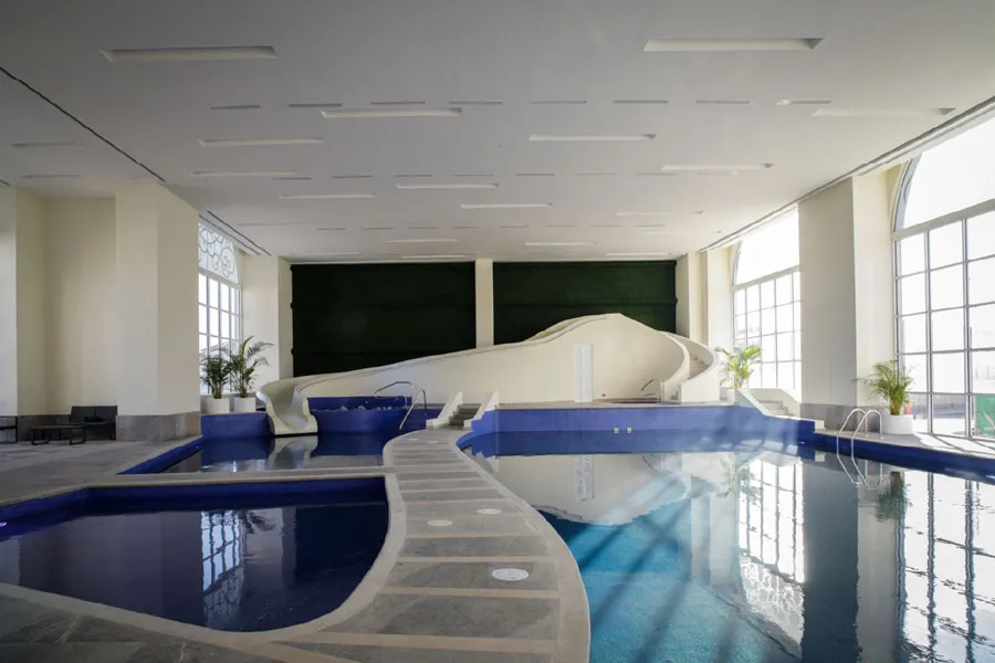 Alberca interior con una escultura blanca curva en el agua y ventanales