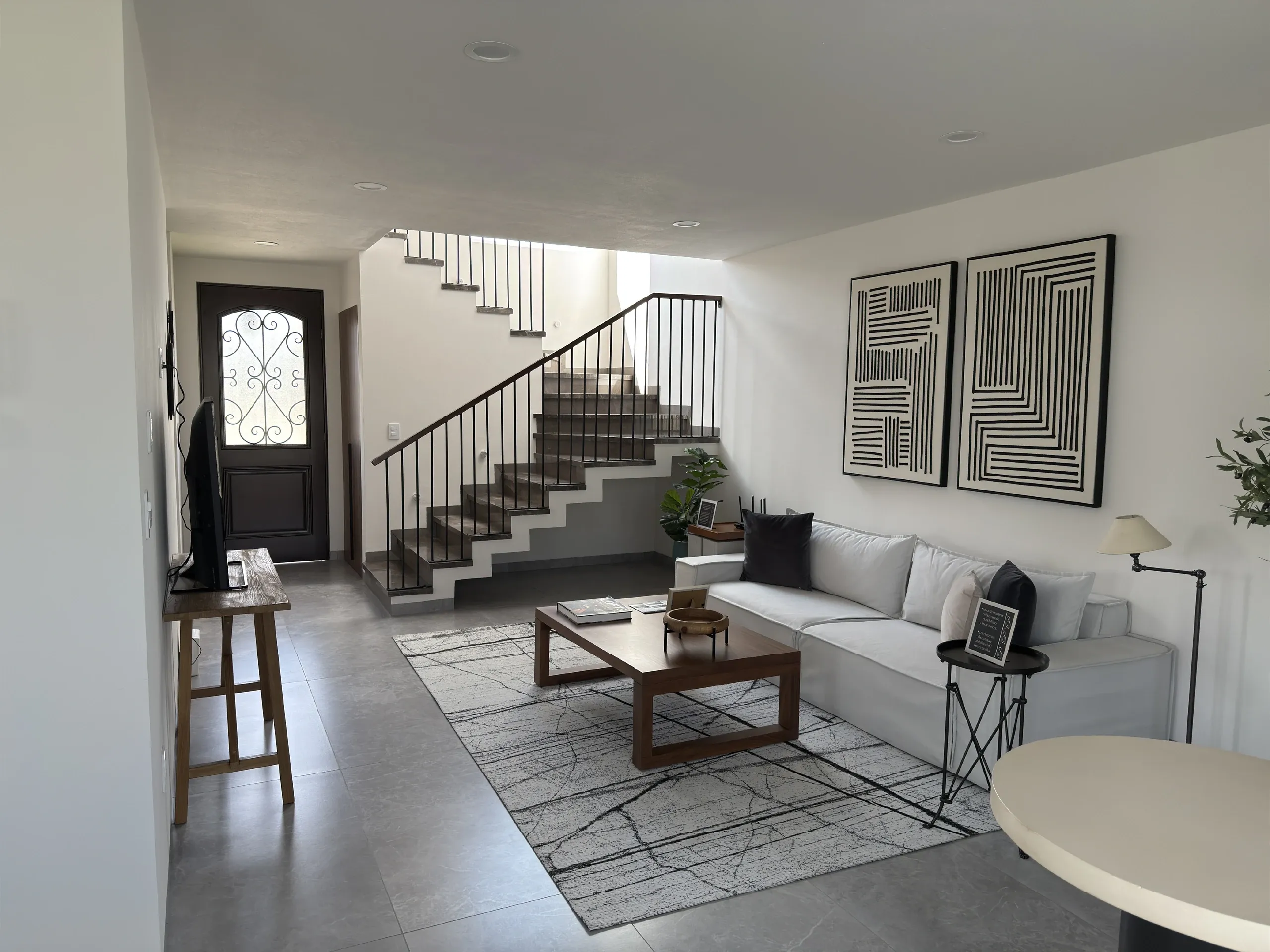 Estancia con sala, escalera con barandal y puerta de acceso con vitral